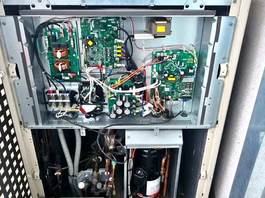 Unidad exterior abierta mostrando sus tarjetas electrónicas y compresor